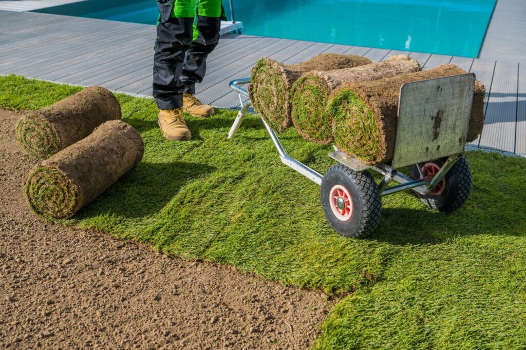 Man standing next to grassy lawn with cart, surrounded by landscape walls and decorative features.