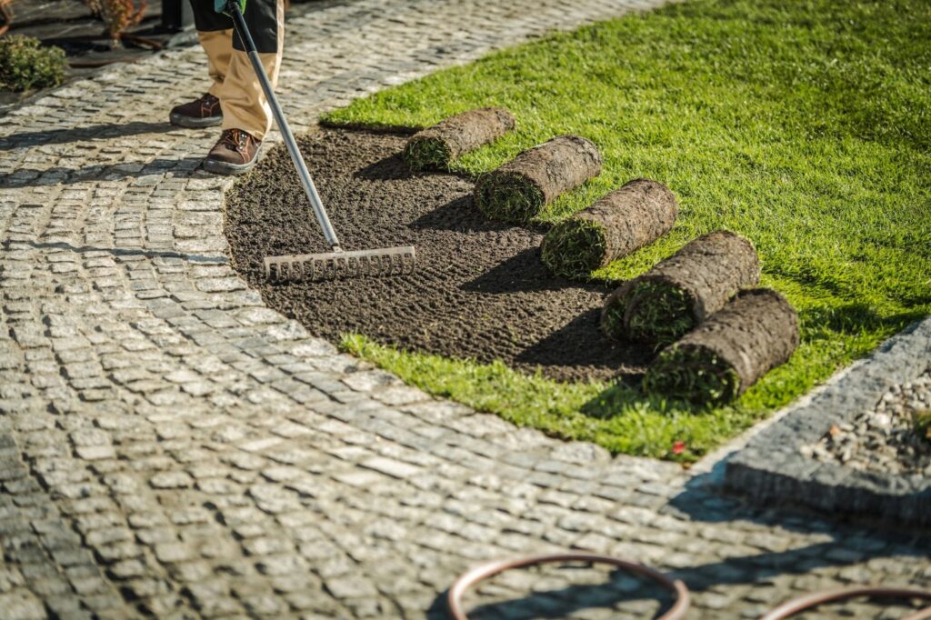 Man using rake to cut grass near landscape walls.