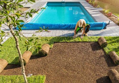 A man tends to a lawn near a pool, showcasing lush grass from Monarch Sod.